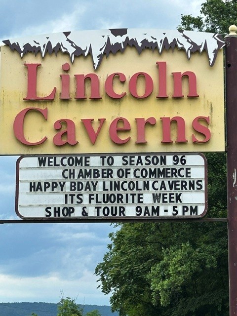 A yellow sign with red letters that read “Lincoln Caverns” and a smaller white sign with black letters describing an event underneath.