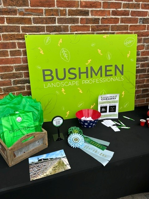 black table with ribbons, pens, goodie bags, pictures and a sign that says “Bushmen Landscaping Professionals” on it.