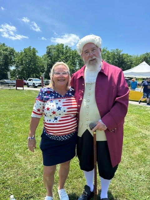 Senator Judy Ward posing for a picture in a grassy area with someone dressed up in a colonial costume.