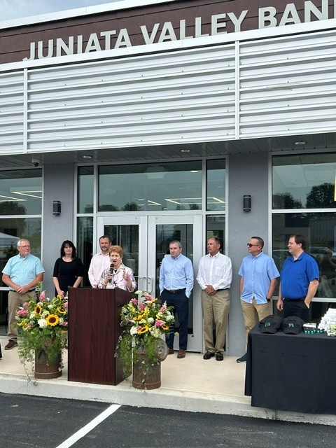 A woman speaking at a podium outside the entrance to a bank with several people standing in a row behind her