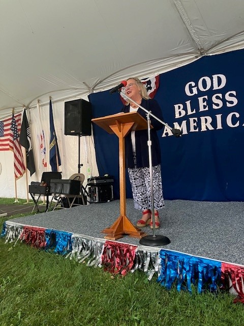 Senator Judy Ward speaking at a podium with a banner behind her that reads “God Bless America”